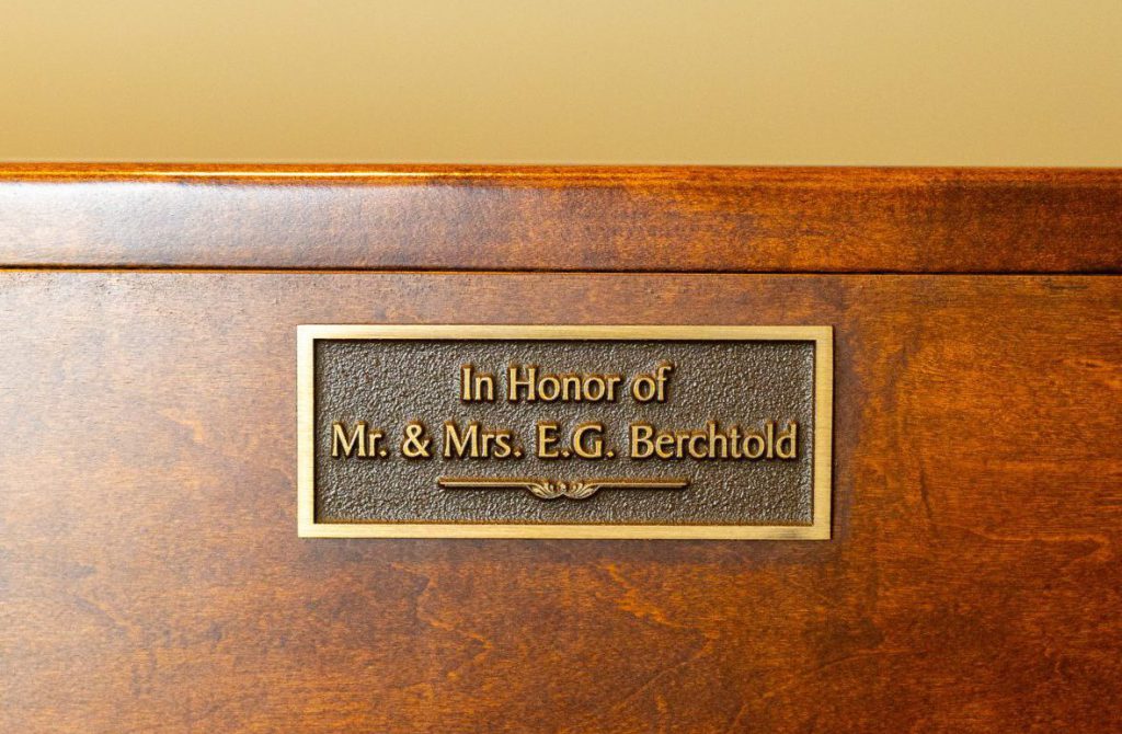 A bronze plaque mounted on a wooden surface, inscribed with 'In Honor of Mr. & Mrs. E.G. Berchtold,' commemorating their contribution or memory.
